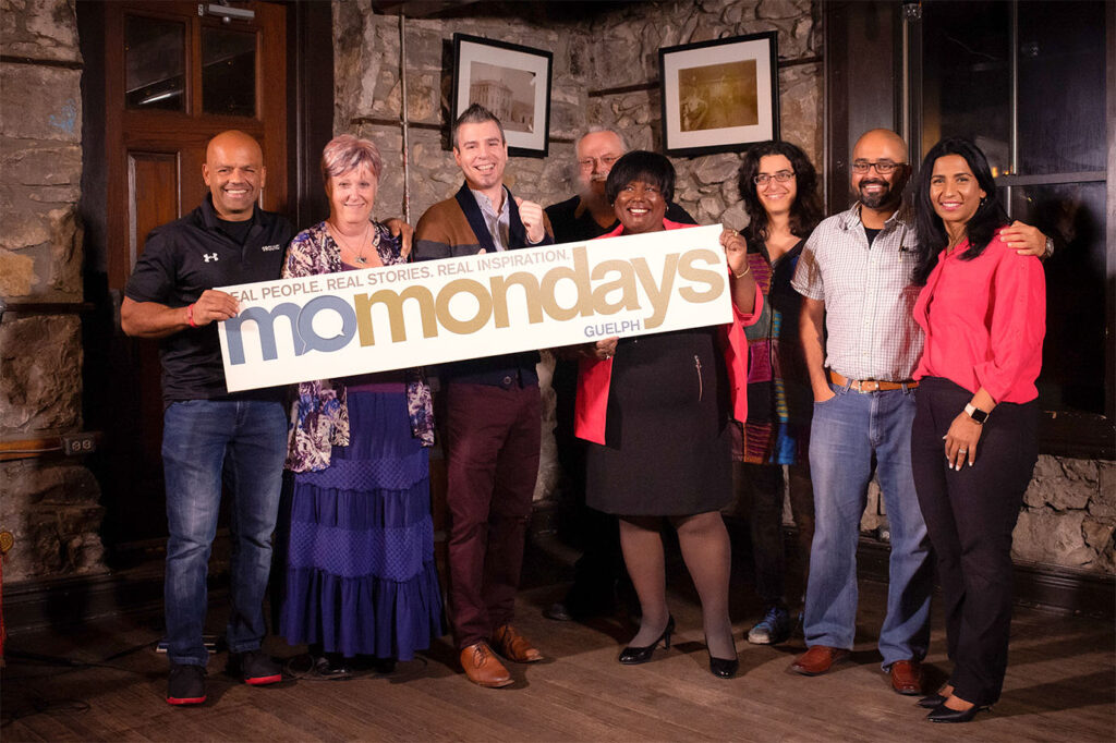 Rob with group of speakers at momondays, holding the momondays sign